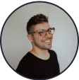 A profile picture of the influencer @blakeasilva. He has short, curly hair, wears glasses and a black t-shirt, and smiles at an off-camera subject.